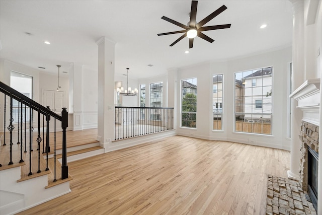 unfurnished living room featuring a stone fireplace, crown molding, light hardwood / wood-style floors, and ceiling fan with notable chandelier