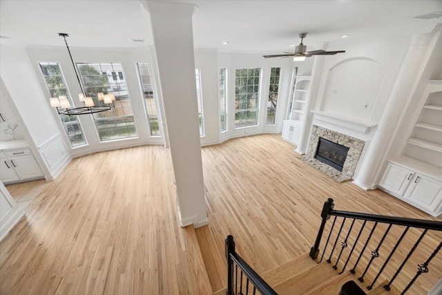 living room with ceiling fan with notable chandelier, light hardwood / wood-style flooring, ornamental molding, built in features, and a fireplace