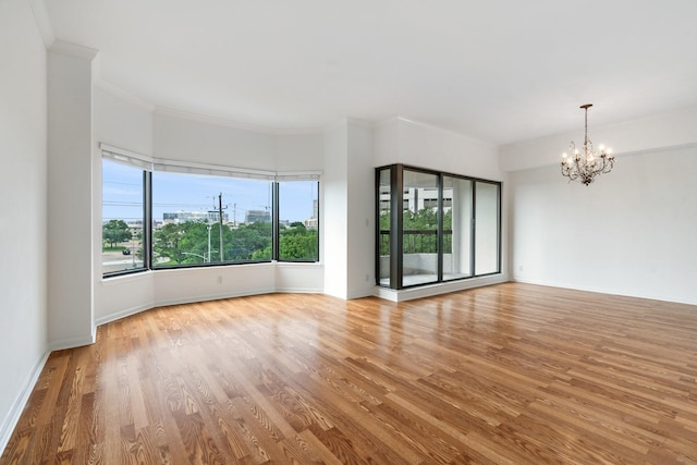 empty room with an inviting chandelier, light wood-type flooring, and ornamental molding