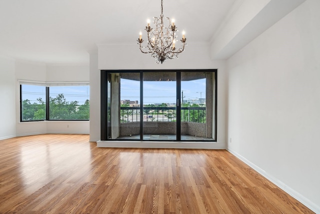 spare room featuring light hardwood / wood-style floors, a notable chandelier, and ornamental molding