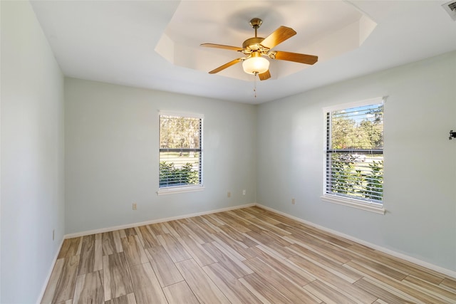 empty room featuring a raised ceiling, ceiling fan, plenty of natural light, and light hardwood / wood-style floors