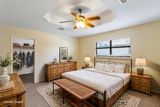 bedroom with light carpet, a tray ceiling, a closet, and ceiling fan