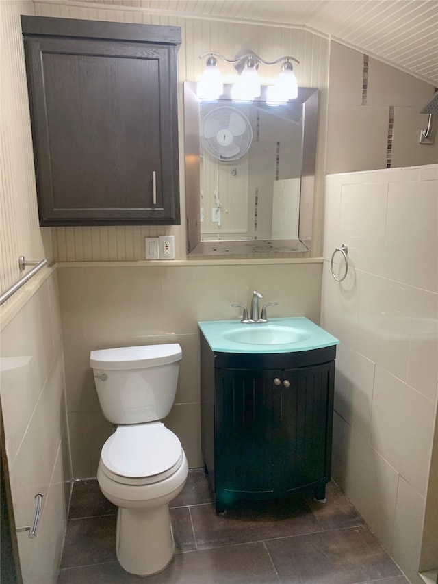 bathroom featuring tile patterned floors, toilet, vaulted ceiling, tile walls, and vanity