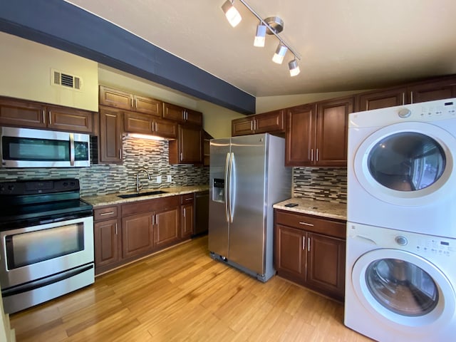 kitchen featuring stacked washer / dryer, stainless steel appliances, decorative backsplash, sink, and light hardwood / wood-style flooring