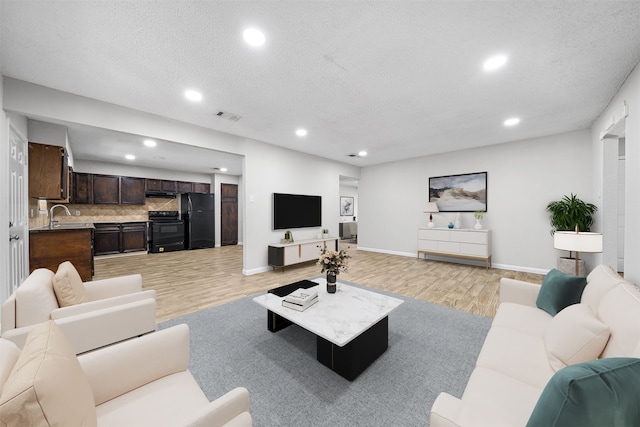 living room featuring sink, a textured ceiling, and light hardwood / wood-style flooring