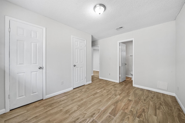 unfurnished bedroom with light hardwood / wood-style flooring, a textured ceiling, and connected bathroom