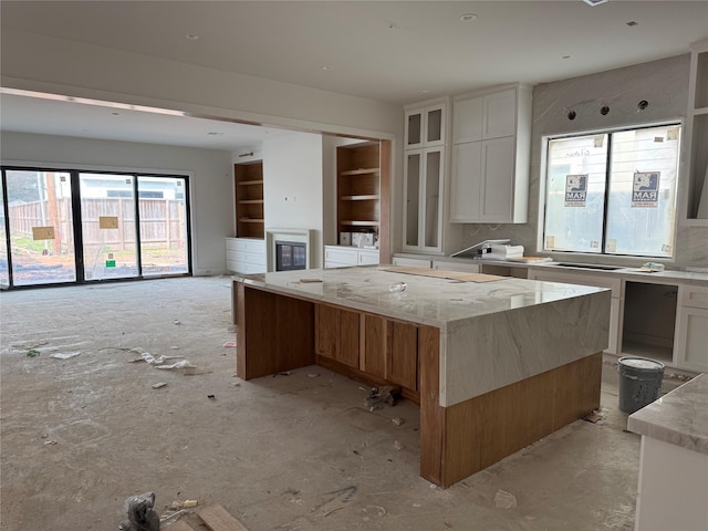 kitchen with light stone counters, white cabinetry, glass insert cabinets, and built in features