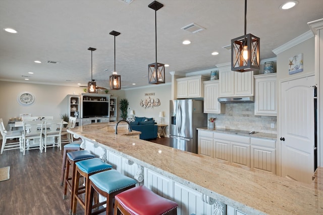 kitchen featuring light stone counters, stainless steel fridge, dark hardwood / wood-style flooring, pendant lighting, and a breakfast bar area