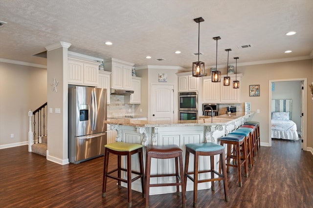 kitchen with dark wood-type flooring, appliances with stainless steel finishes, a breakfast bar area, and hanging light fixtures