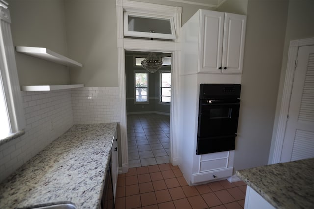 kitchen with dark tile patterned floors, light stone countertops, an inviting chandelier, white cabinets, and oven