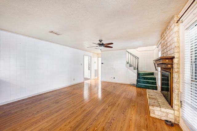 unfurnished living room with light hardwood / wood-style floors, ceiling fan, a textured ceiling, and a large fireplace