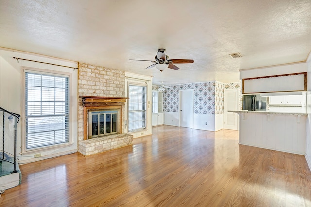 unfurnished living room featuring a brick fireplace, ceiling fan, a textured ceiling, and light wood-type flooring