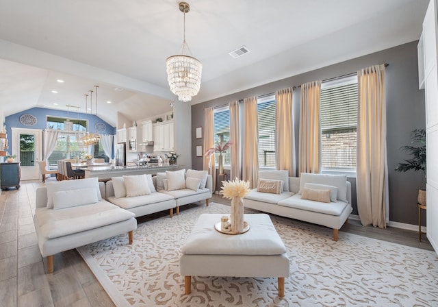 living room with an inviting chandelier, a wealth of natural light, vaulted ceiling, and light hardwood / wood-style floors