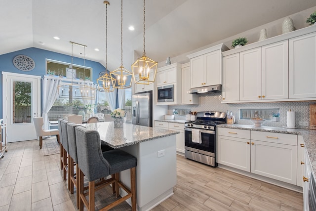 kitchen with light stone counters, stainless steel appliances, hanging light fixtures, vaulted ceiling, and white cabinets