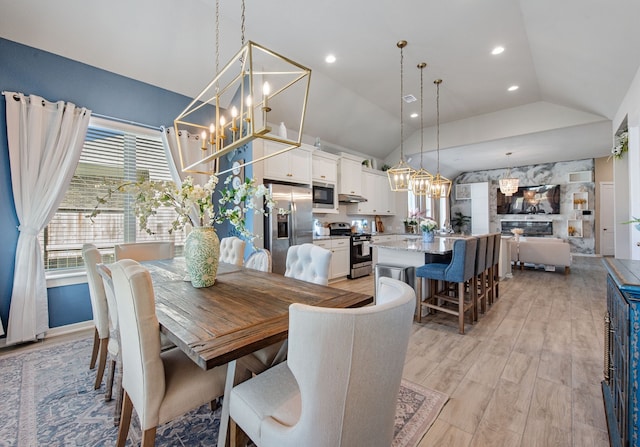 dining room featuring light wood-type flooring, a fireplace, and vaulted ceiling