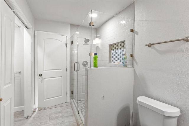 bathroom with hardwood / wood-style floors, an enclosed shower, and toilet