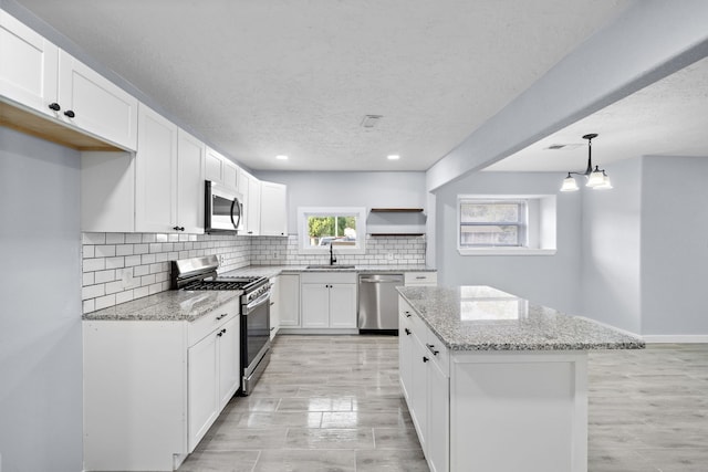 kitchen featuring white cabinets, hanging light fixtures, sink, light stone countertops, and appliances with stainless steel finishes