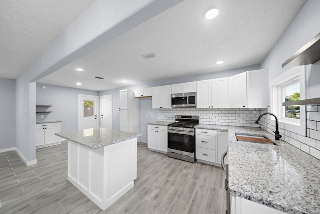 kitchen featuring white cabinetry, sink, light stone counters, appliances with stainless steel finishes, and a center island