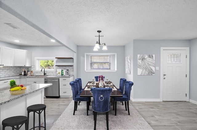 dining area featuring sink, a textured ceiling, a notable chandelier, and light hardwood / wood-style flooring