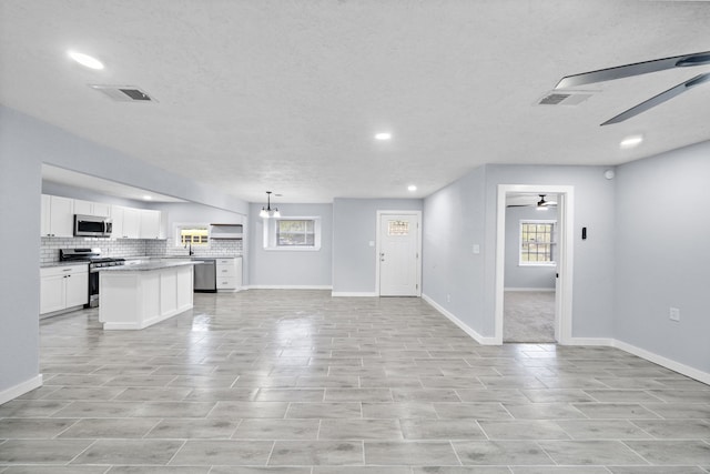 kitchen featuring white cabinetry, appliances with stainless steel finishes, a textured ceiling, hanging light fixtures, and a center island