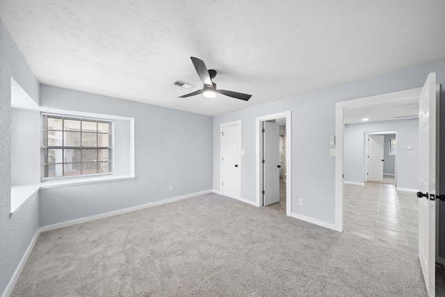 unfurnished bedroom with a textured ceiling, light carpet, ceiling fan, and ensuite bathroom