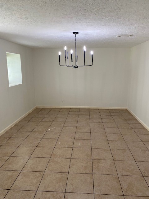 tiled spare room with a textured ceiling and a chandelier