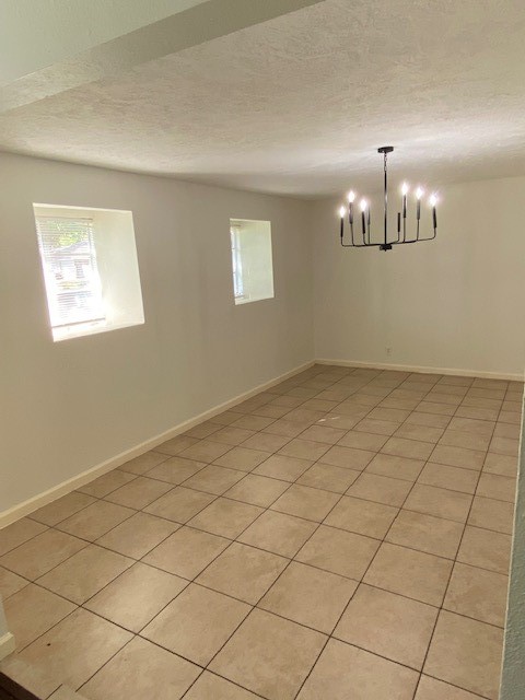 tiled empty room with a chandelier and a textured ceiling