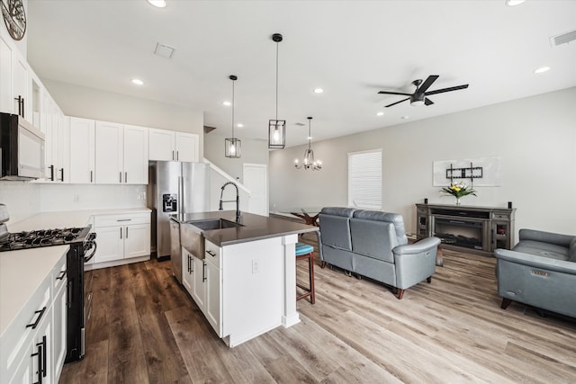 kitchen with white cabinetry, sink, black gas range, an island with sink, and hardwood / wood-style floors