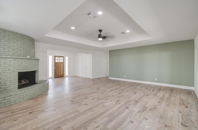 unfurnished living room with ceiling fan, a tray ceiling, and light hardwood / wood-style floors