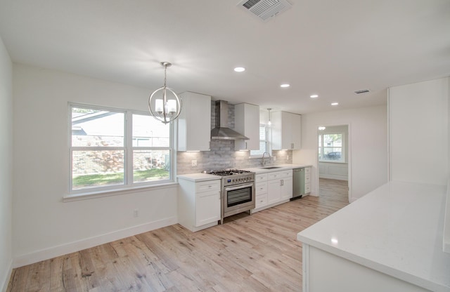 kitchen featuring stainless steel appliances, wall chimney range hood, decorative light fixtures, white cabinets, and light hardwood / wood-style flooring