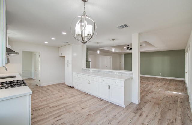 kitchen with white cabinets, wall chimney range hood, light wood-type flooring, and decorative light fixtures