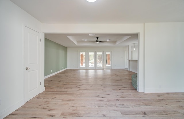 unfurnished room with ceiling fan, a raised ceiling, light wood-type flooring, and french doors