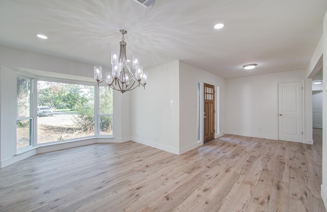 empty room with light wood-type flooring and a notable chandelier