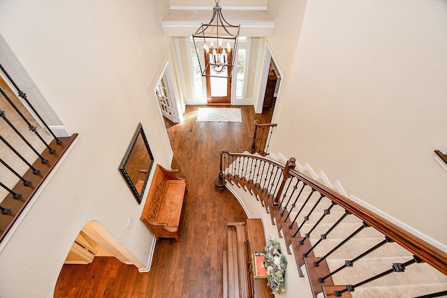 staircase with a high ceiling, a notable chandelier, and hardwood / wood-style flooring