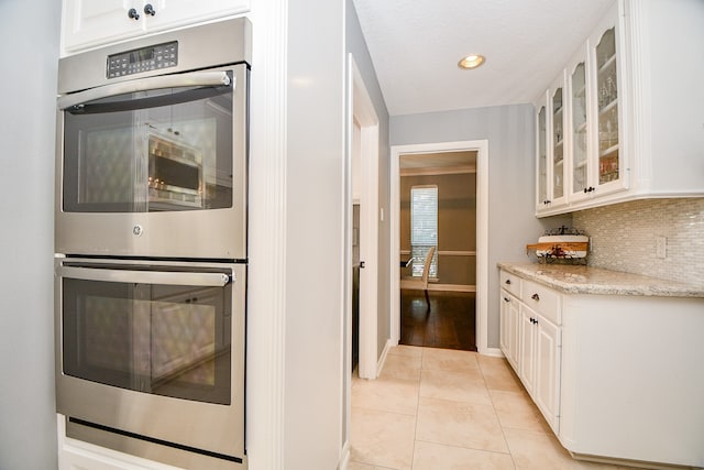 kitchen featuring backsplash, white cabinets, light tile patterned floors, light stone counters, and stainless steel double oven