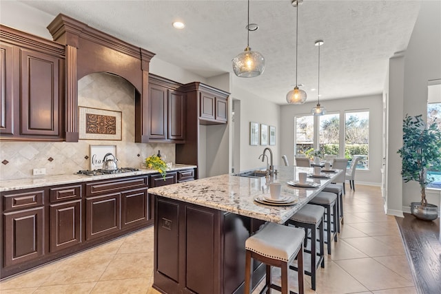 kitchen with sink, hanging light fixtures, decorative backsplash, a center island with sink, and light tile patterned floors