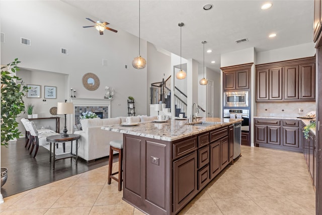 kitchen with a kitchen island with sink, hanging light fixtures, ceiling fan, light tile patterned floors, and appliances with stainless steel finishes