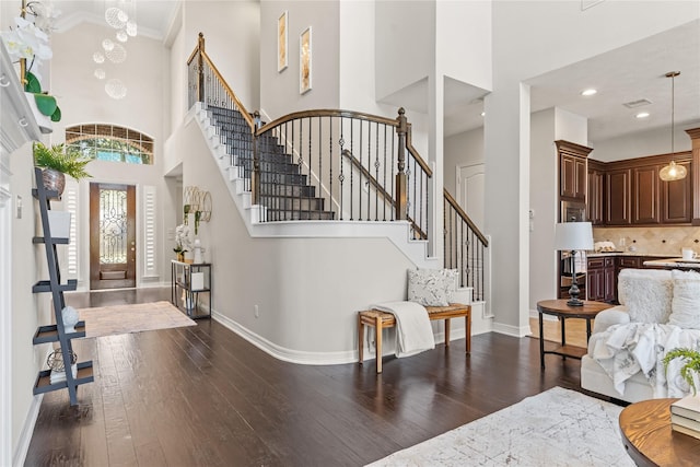 entryway with an inviting chandelier, a towering ceiling, dark wood-type flooring, and ornamental molding