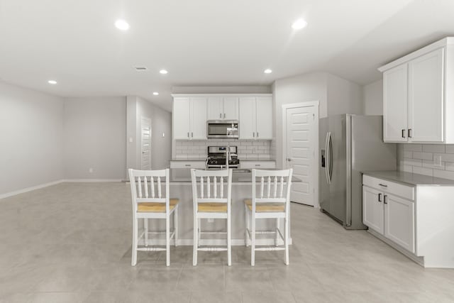 kitchen with white cabinets, a kitchen island with sink, backsplash, a breakfast bar, and appliances with stainless steel finishes