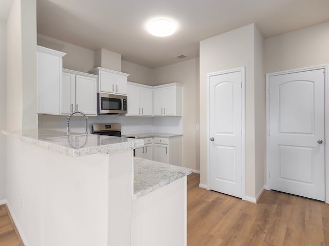 kitchen with light stone counters, white cabinetry, appliances with stainless steel finishes, kitchen peninsula, and light hardwood / wood-style flooring