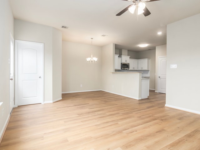 unfurnished living room featuring ceiling fan with notable chandelier and light hardwood / wood-style flooring