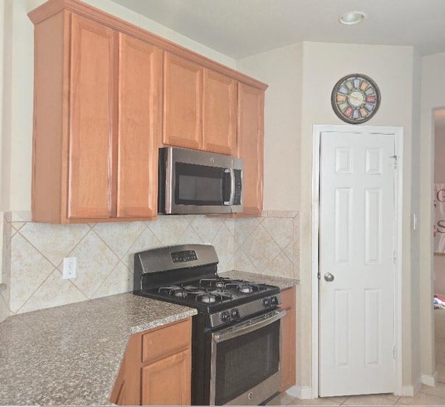 kitchen featuring stainless steel appliances, dark stone countertops, light tile patterned floors, and decorative backsplash