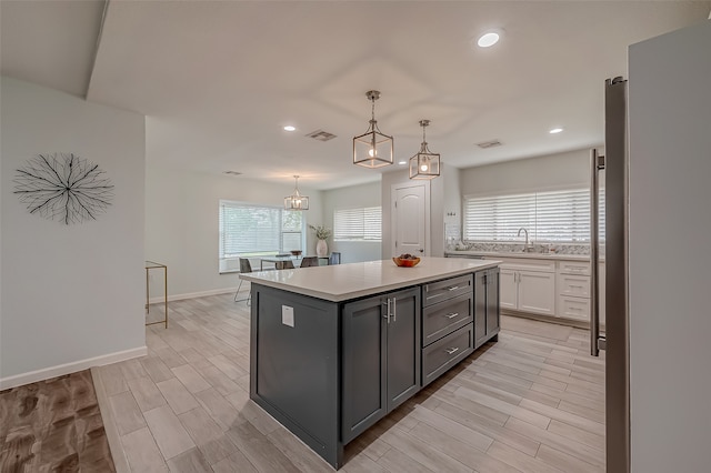 kitchen with white cabinets, light wood-type flooring, decorative light fixtures, and a center island