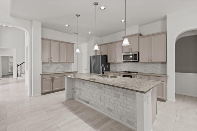 kitchen with light stone countertops, sink, decorative light fixtures, a center island with sink, and appliances with stainless steel finishes