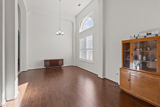 unfurnished dining area featuring an inviting chandelier, dark hardwood / wood-style flooring, and a towering ceiling