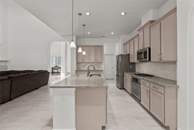 kitchen featuring an island with sink, stainless steel appliances, sink, light stone counters, and pendant lighting