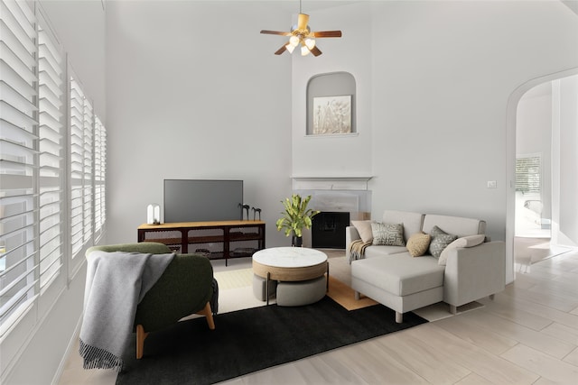 living room with ceiling fan, a towering ceiling, a wealth of natural light, and light wood-type flooring