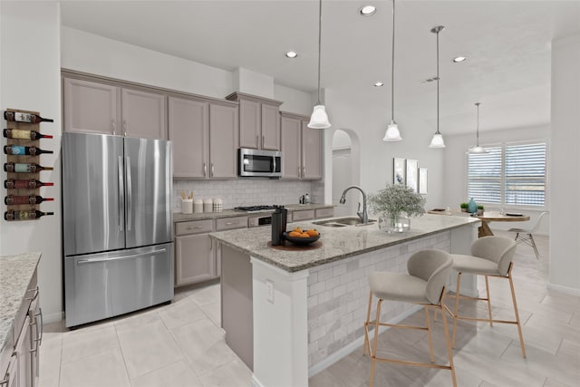 kitchen with a center island with sink, sink, stainless steel appliances, and hanging light fixtures