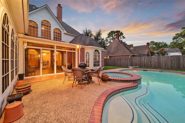 pool at dusk featuring a patio and an in ground hot tub