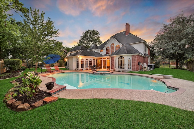 pool at dusk with a diving board, a lawn, an in ground hot tub, and a patio area